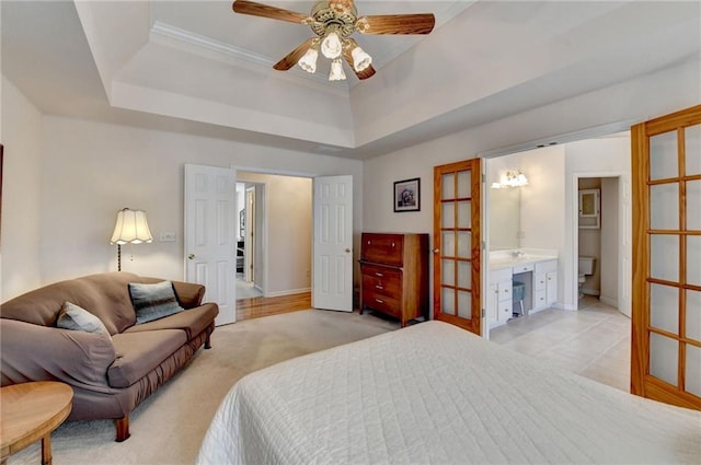 bedroom featuring a raised ceiling, connected bathroom, baseboards, and light carpet