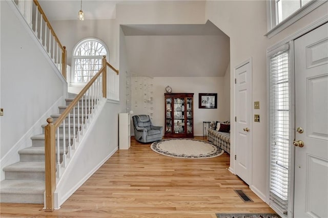 foyer entrance featuring a towering ceiling, light wood-style flooring, and stairs