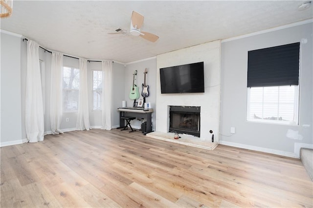 living room with a fireplace, crown molding, a wealth of natural light, and light wood-type flooring