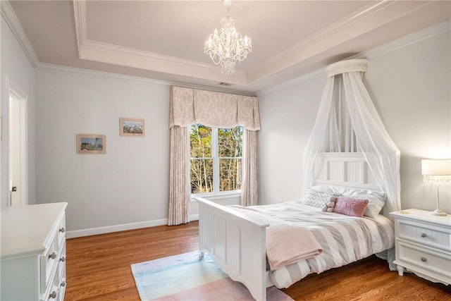 bedroom with a tray ceiling, crown molding, light hardwood / wood-style flooring, and an inviting chandelier