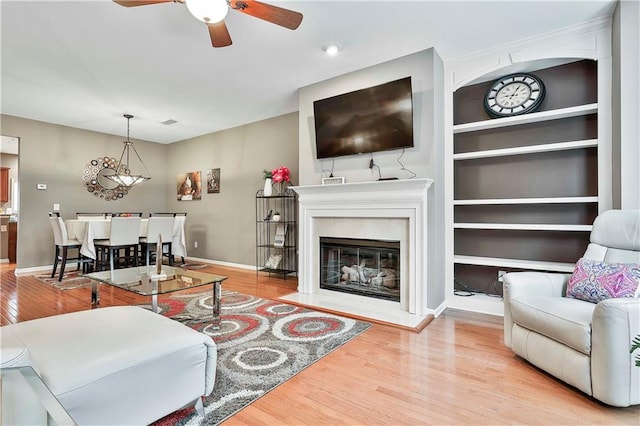 living room featuring built in features, a glass covered fireplace, baseboards, and wood finished floors