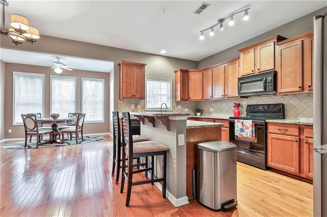 kitchen featuring visible vents, a kitchen breakfast bar, a center island, light wood-type flooring, and black appliances