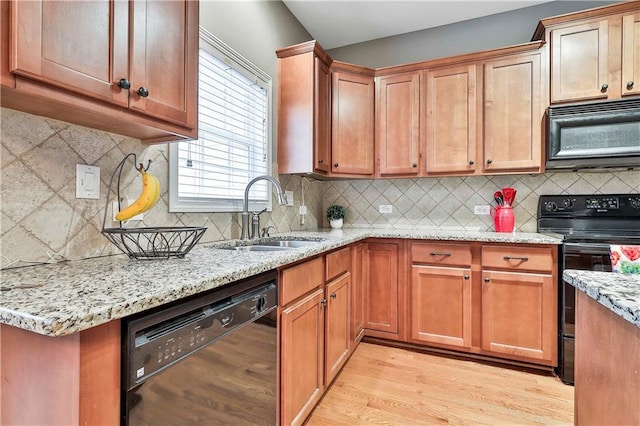 kitchen featuring a sink, light wood-type flooring, light stone countertops, black appliances, and tasteful backsplash