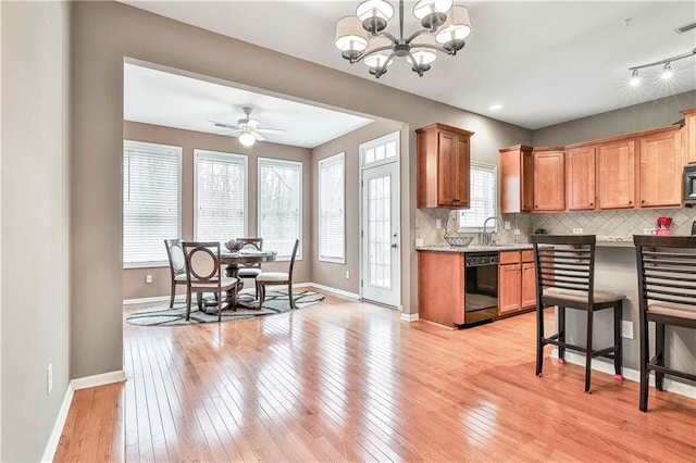 kitchen featuring light wood finished floors, tasteful backsplash, baseboards, dishwasher, and ceiling fan with notable chandelier