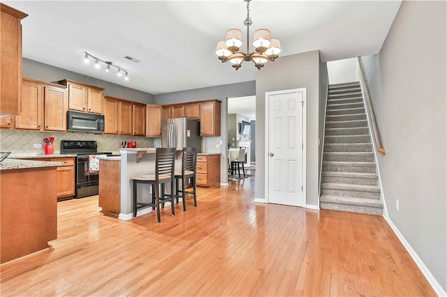 kitchen featuring light wood finished floors, a breakfast bar area, light countertops, black appliances, and backsplash