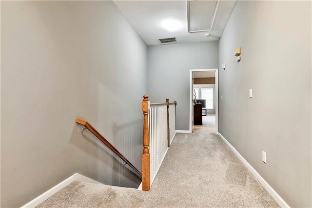 hallway featuring attic access, baseboards, visible vents, carpet flooring, and an upstairs landing