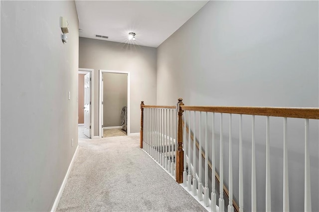 hallway featuring carpet, visible vents, baseboards, and an upstairs landing