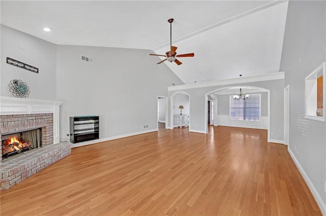 unfurnished living room featuring lofted ceiling, light wood-type flooring, ceiling fan with notable chandelier, and a fireplace