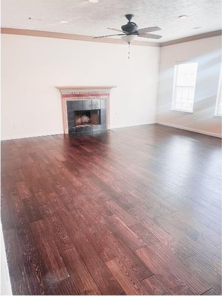 unfurnished living room featuring dark hardwood / wood-style flooring, a textured ceiling, ceiling fan, crown molding, and a tile fireplace