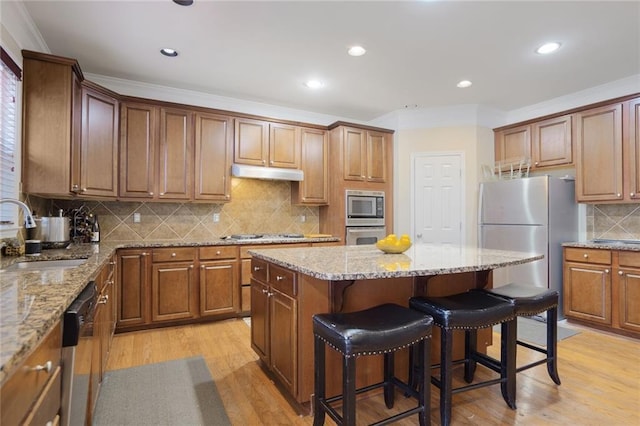 kitchen with a sink, ornamental molding, stainless steel appliances, under cabinet range hood, and a kitchen island