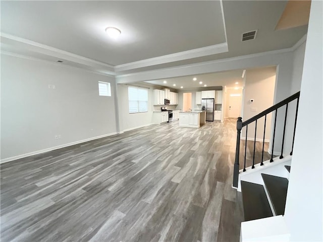 unfurnished living room with baseboards, visible vents, stairway, wood finished floors, and crown molding