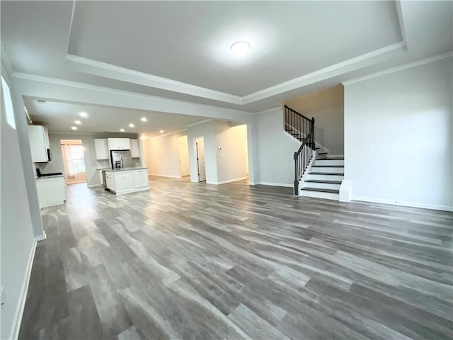 unfurnished living room featuring ornamental molding, a tray ceiling, stairway, and wood finished floors