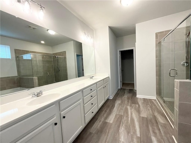 full bathroom with double vanity, visible vents, a sink, a shower stall, and wood finished floors