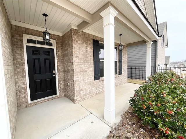 view of exterior entry with a porch, brick siding, and fence