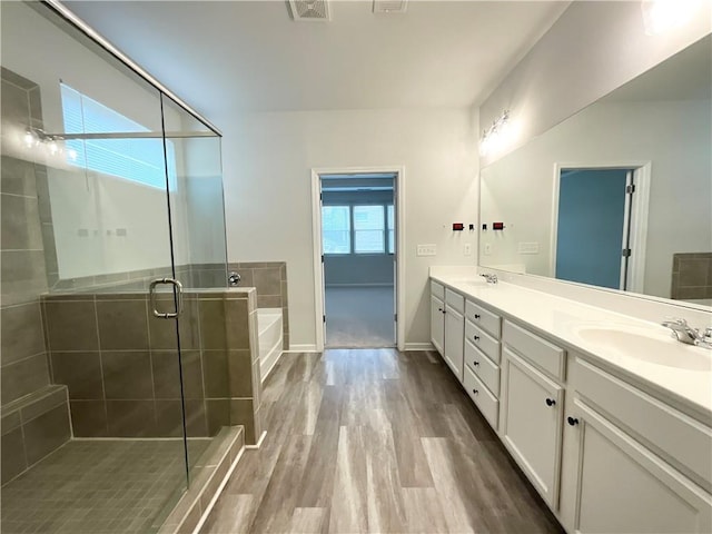 bathroom featuring a stall shower, wood finished floors, a sink, and double vanity