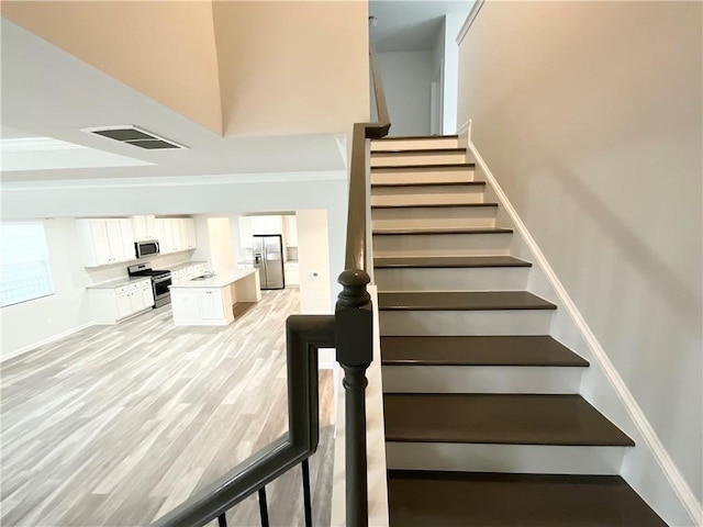 stairs with baseboards, visible vents, a high ceiling, and wood finished floors