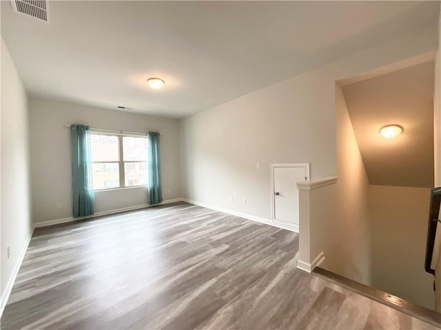 empty room featuring wood finished floors, visible vents, and baseboards