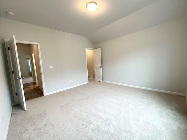 unfurnished bedroom with lofted ceiling, baseboards, and light colored carpet