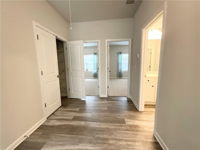 corridor featuring visible vents, baseboards, and wood finished floors