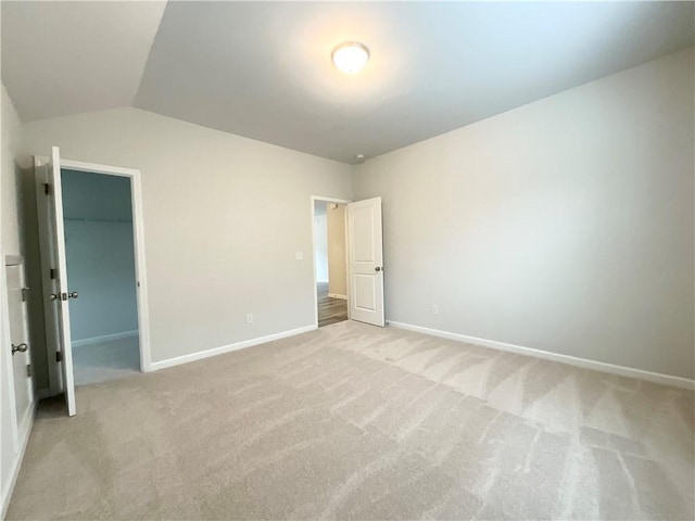 interior space featuring a walk in closet, a closet, light colored carpet, vaulted ceiling, and baseboards