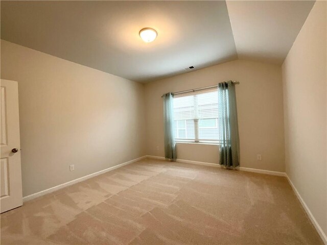 spare room with light carpet, vaulted ceiling, and baseboards