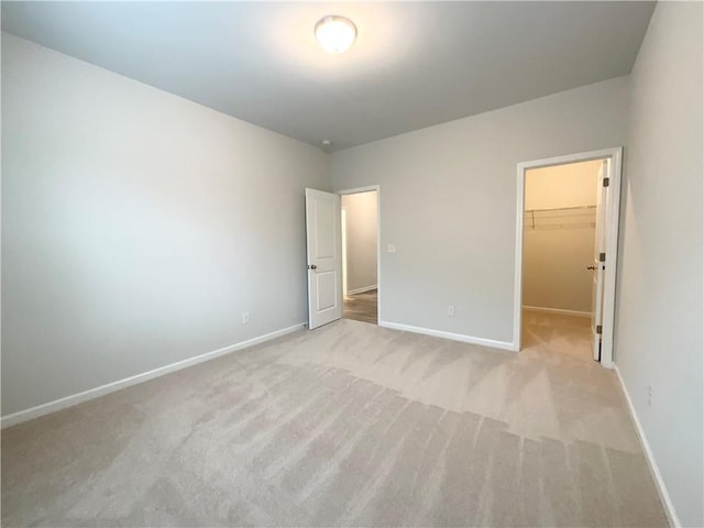 unfurnished bedroom with light carpet, a spacious closet, and baseboards