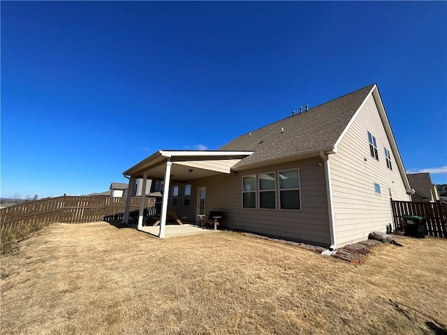 back of property with a patio, a yard, roof with shingles, and a fenced backyard