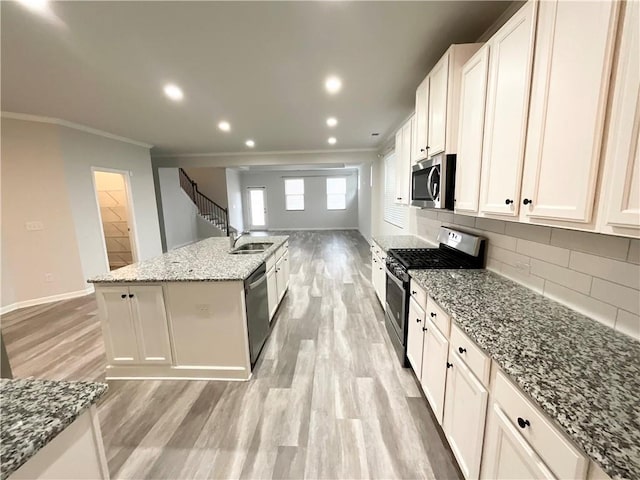 kitchen featuring a kitchen island with sink, stainless steel appliances, ornamental molding, light wood-type flooring, and tasteful backsplash