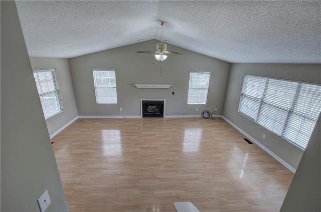 unfurnished living room featuring a wealth of natural light, light hardwood / wood-style floors, ceiling fan, and vaulted ceiling