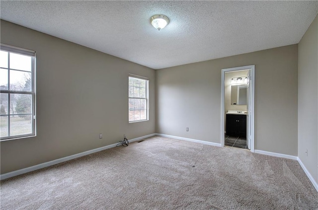 unfurnished bedroom with ensuite bath, light carpet, and a textured ceiling