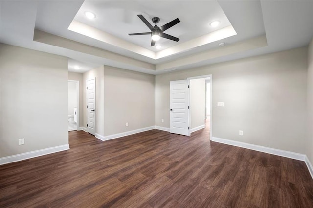 spare room with ceiling fan, a tray ceiling, and dark hardwood / wood-style flooring