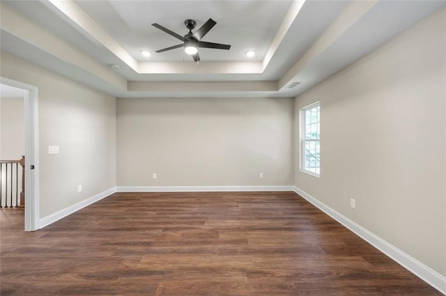 unfurnished room featuring dark wood-type flooring, a raised ceiling, and ceiling fan