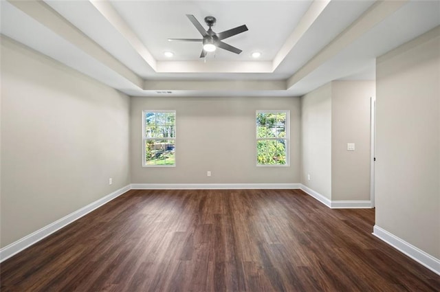 unfurnished room with a healthy amount of sunlight, dark wood-type flooring, ceiling fan, and a tray ceiling