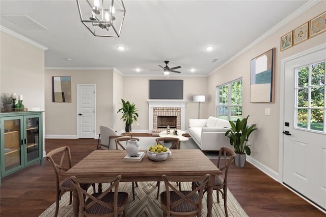 dining space featuring ceiling fan with notable chandelier, ornamental molding, dark wood-type flooring, and a fireplace