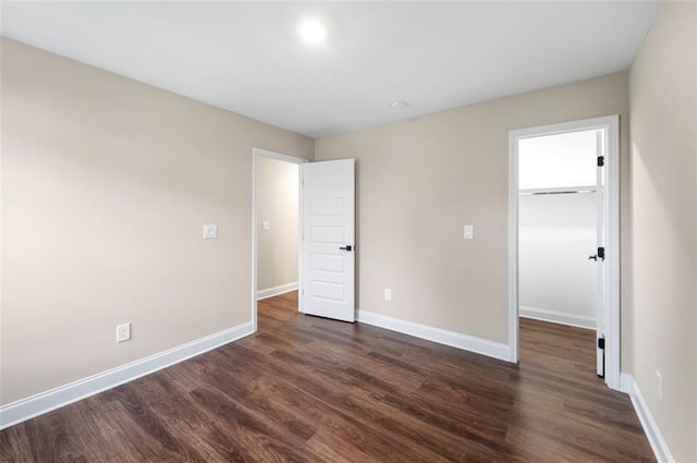 unfurnished bedroom with a walk in closet, a closet, and dark wood-type flooring