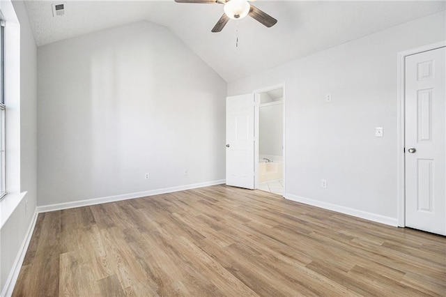 unfurnished bedroom with light wood-type flooring, baseboards, vaulted ceiling, and connected bathroom