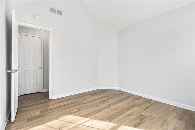 spare room with lofted ceiling, light wood-style flooring, visible vents, and baseboards