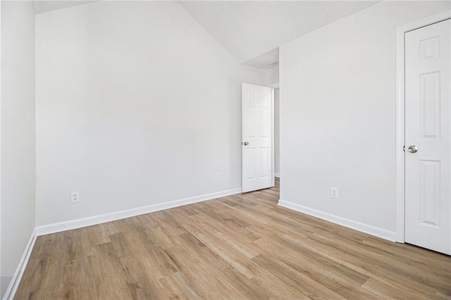 unfurnished bedroom featuring baseboards, lofted ceiling, and light wood-style floors