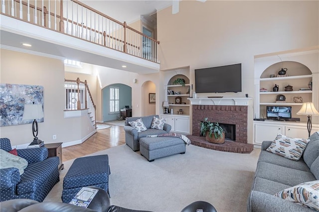 living area featuring built in shelves, stairway, arched walkways, baseboards, and a brick fireplace