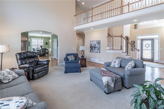 living area featuring ornamental molding, arched walkways, baseboards, a towering ceiling, and stairs