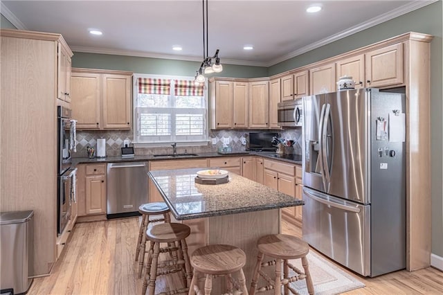 kitchen featuring a breakfast bar, light brown cabinetry, a sink, stainless steel appliances, and crown molding