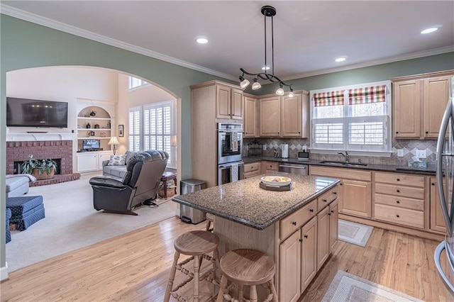 kitchen with a breakfast bar, a sink, ornamental molding, stainless steel appliances, and open floor plan