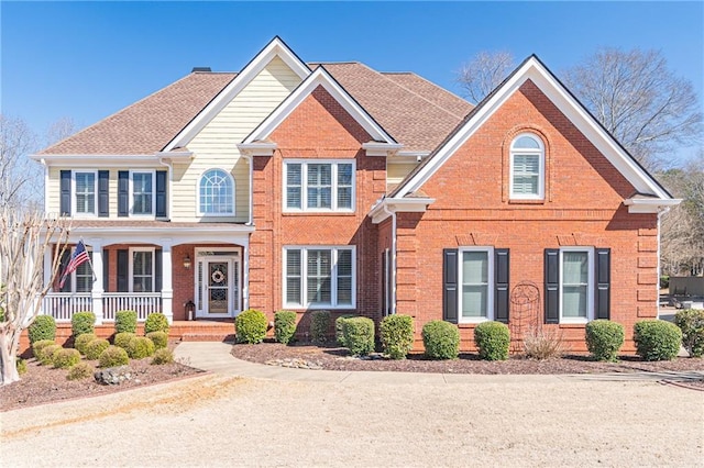 view of front of home with brick siding, covered porch, and a shingled roof