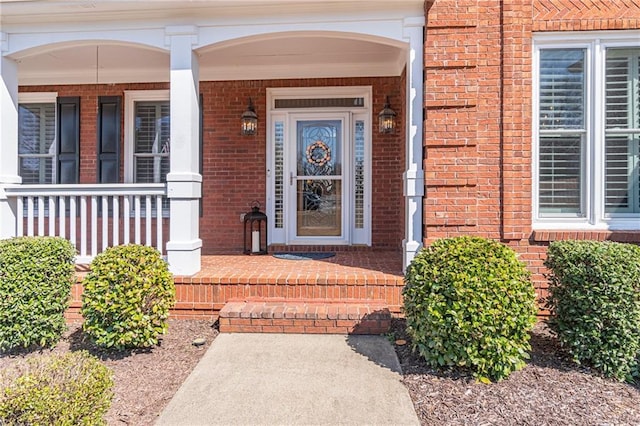 view of exterior entry featuring brick siding and a porch