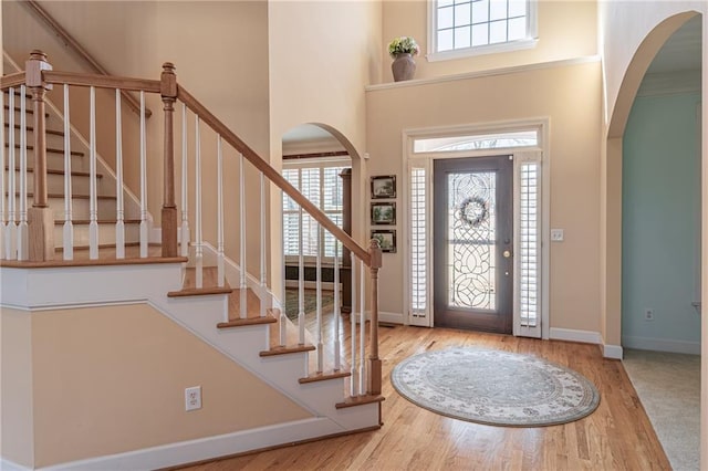 foyer with arched walkways, baseboards, a towering ceiling, and wood finished floors