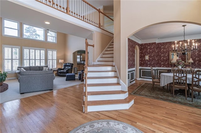 stairway featuring wood finished floors, wallpapered walls, an inviting chandelier, arched walkways, and crown molding