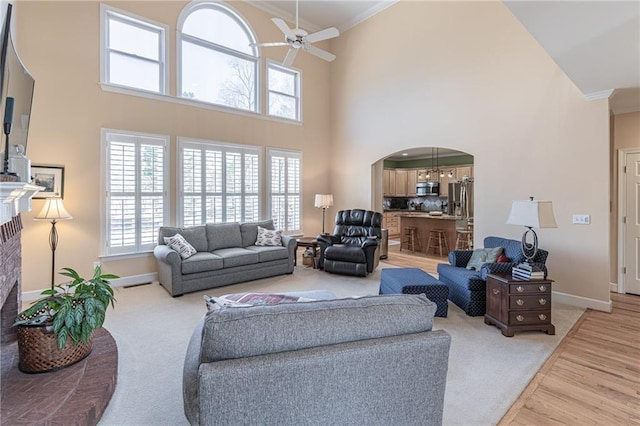 living area featuring ornamental molding, arched walkways, light wood finished floors, baseboards, and ceiling fan