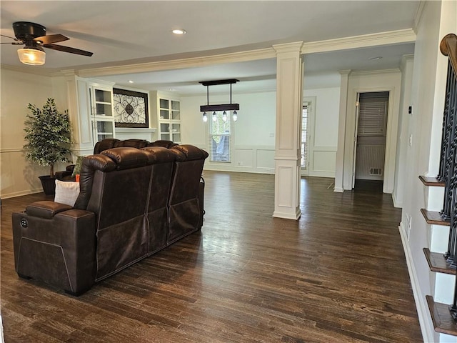 living area with decorative columns, dark wood finished floors, crown molding, and a decorative wall