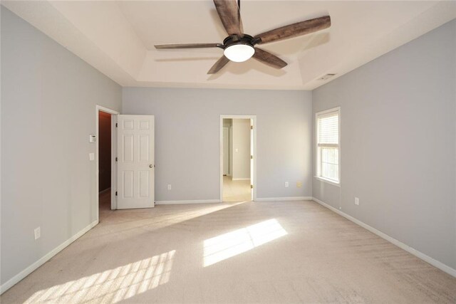 unfurnished bedroom featuring ceiling fan, a raised ceiling, and light carpet