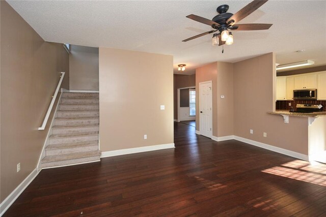 unfurnished living room featuring ceiling fan, dark hardwood / wood-style flooring, and a textured ceiling